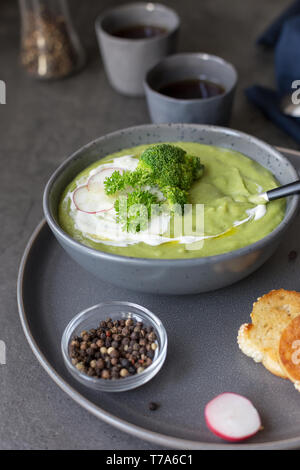 Vue de côté l'alimentation soupe crème de brocoli et de crème sure avec radis, spoon, le poivre et une serviette près de béton sur fond gris. Concept de l'alimentation de l'été Banque D'Images