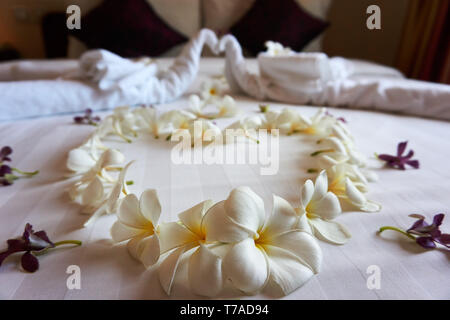 Plumeria Fleurs disposées en forme de cœur, et les serviettes disposées en deux cygnes s'embrasser sur un lit dans un luxueux hôtel Gloria Angkor au Cambodge. Banque D'Images