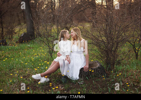 Mère et enfant sont vous détendre sur la prairie parmi les fleurs. Fille est assise dans les genoux de sa mère. Du temps ensemble. La Fête des mères. Mère et fille regardant Banque D'Images