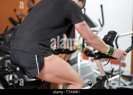 Vtt homme musclé dans la salle de sport, l'exercice de jambes faisant cardio vélo, vélos spinning class . Banque D'Images
