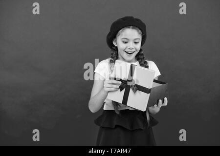 Cadeau de Noël pour fille. Petite fille mignonne reçu cadeau de vacances. Meilleurs cadeaux de Noël. Enfant heureux de déballer son cadeau. Kid petite fille tenir boîte-cadeau avec ruban sur fond rouge. Banque D'Images