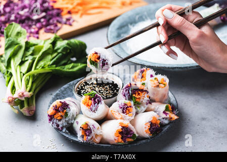 La cuisine asiatique de manger des rouleaux de printemps ou des rouleaux de papier de riz avec légumes et les crevettes. Rouleau de maintien à la main avec des baguettes Banque D'Images