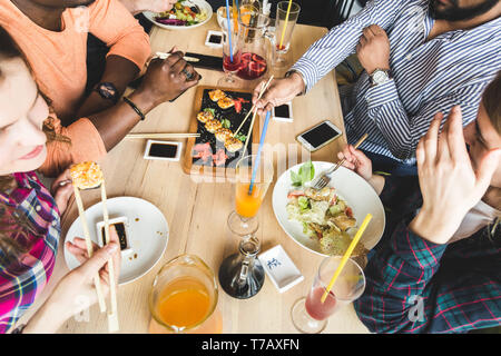 Vue d'en haut. Une société multiculturelle de l'entreprise des jeunes dans un café de manger des sushis rolls, boire un verre d'avoir du plaisir. Banque D'Images