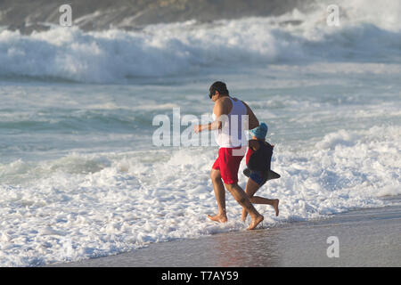 Un père et sa jeune fille en vacances de vacances de détente ayant du plaisir à courir dans la mer à Fistral Beach à Newquay dans les Cornouailles. Banque D'Images