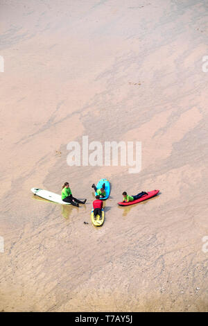 Les jeunes vacanciers, à l'écoute de leur instructeur de surf pendant une leçon de surf sur la grande plage de l'Ouest à Newquay en Cornouailles. Banque D'Images
