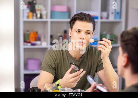 Beau jeune homme aux cheveux noirs appliquant le maquillage sur le visage Banque D'Images