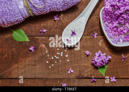 Composition de Spa et de bien-être avec de l'eau fleurs lilas parfumés dans un bol, du sel de mer et de l'absorbant sur fond de bois. L'aromathérapie pour votre détente, vue du dessus Banque D'Images