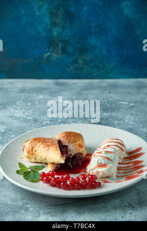 Des tranchées d'un strudel aux fruits rouges frais servi avec des baies de cassis et le sucre en poudre sur une vieille plaque de fond sur un pic avec de la crème glacée Banque D'Images