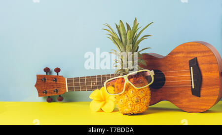 L'ananas mûr jaune en lunettes de soleil. La guitare sur fond bleu jaune. Mordashkaiz drôle de fruits tropicaux. Concept Banque D'Images