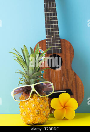 L'ananas mûr jaune en lunettes de soleil. La guitare sur fond bleu jaune. Mordashkaiz drôle de fruits tropicaux. Concept Banque D'Images