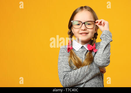 Portrait of a cute little kid girl à lunettes sur un fond jaune. Écolière de l'enfant regardant la caméra. Le concept de l'éducation. Copier l'espace. Banque D'Images