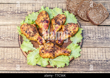 Cuisses de poulet grillées et de feuilles de laitue sur planche à découper en bois, de pain noir avec des graines de tournesol sur la surface en bois. Banque D'Images