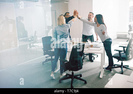 Groupe de travail diversifié sourire collègues debout autour d'une table de bureau et de l'autre, on subit donc élevé au cours d'une réunion Banque D'Images