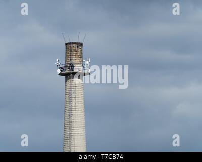 Grande cheminée d'usine en briques blanches. Fer à repasser degrés mènent à la partie supérieure. Il y a des antennes paraboliques sur la cheminée. Il y a deux personnes travaillant sur Banque D'Images