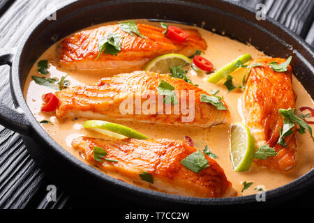 Filet de saumon d'offres dans la noix de coco Thaï curry avec de la chaux et des herbes close-up dans une casserole sur la table horizontale. Banque D'Images