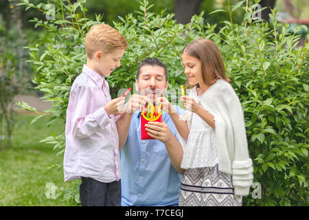 Smiling père et enfants de manger des légumes frais dans la nature - heureux papa holding poivrons colorés en forme de frites pour les enfants Banque D'Images