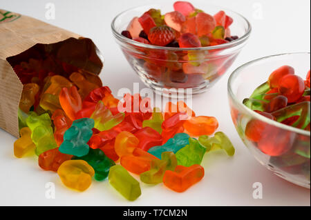 Bols en verre et sac de papier de bonbons gommeux colorés sur fond blanc Banque D'Images