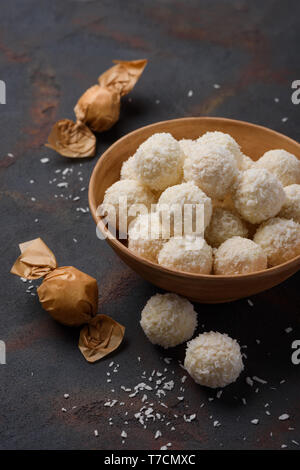 Bonbons de coco dans un bol et enroulé sur le tableau sombre contexte Banque D'Images