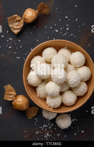 Bonbons de coco dans un bol et enveloppés dans des sombres sur fond de table télévision jeter vue supérieure Banque D'Images