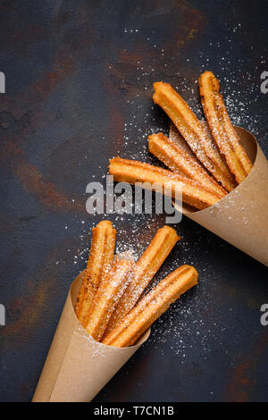 Churros sticks douce chaude avec du sucre en poudre et la cannelle en sac de papier sur fond sombre vue de dessus Banque D'Images