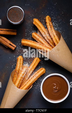 Churros avec du sucre en poudre avec une sauce au chocolat et des bâtons de cannelle sur fond sombre vue de dessus Banque D'Images