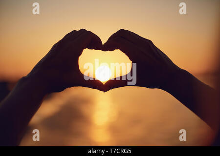 Mains en forme de cœur sur le coucher du soleil au bord de la mer. Banque D'Images