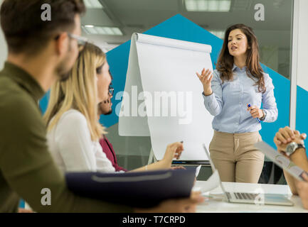 Certains jeunes chef d'équipe en donnant une présentation à un groupe de jeunes collègues, assis, regroupées par le tableau de conférence dans le petit bureau de démarrage Banque D'Images