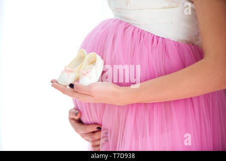 Heureuse fête en prévision de la naissance de sa fille. Pregnant woman holding baby booties sneakers sur fond de ventre. Close-up of a pregnant belly. Banque D'Images