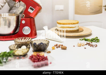 Jeune femme pâtissier bat la crème dans un bol en métal rouge dans un mélangeur électrique. Le concept de pâtisserie maison, la cuisine Banque D'Images