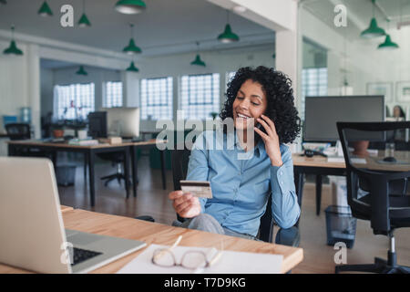 Smiling businesswoman en utilisant sa carte de crédit par téléphone Banque D'Images