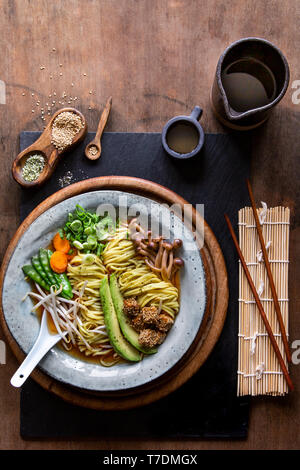 Vegan soupe ramen japonais avec de l'avocat, de sésame le tofu et les champignons en gris bol sur fond de bois Banque D'Images