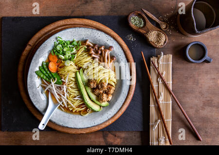 Vegan soupe ramen japonais avec de l'avocat, de sésame le tofu et les champignons en gris bol sur fond de bois Banque D'Images