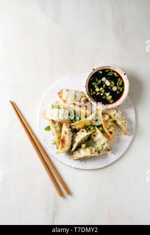 Les Gyozas frits boulettes asiatiques potstickers dans une plaque en céramique blanc servi avec des baguettes et un bol de sauce de soja sur l'oignon blanc en arrière-plan. Télévision Banque D'Images