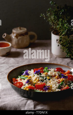 Salade de couscous aux légumes étuvé bébés carottes, haricots verts, maïs doux, les épinards dans une plaque en céramique avec des tomates, de sésame et de fleurs comestibles, plateau Banque D'Images