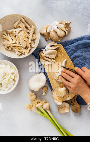 Woman slicing pleurotes sur une planche de bois. Les oignons et l'ail frais accompagner. Banque D'Images