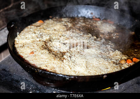 Pour la cuisson du riz pilaw ou paella dans chaudron en fer sur feu ouvert. La fumée et la vapeur. La préparation des aliments savoureux processus extérieur arrière-plan. Banque D'Images