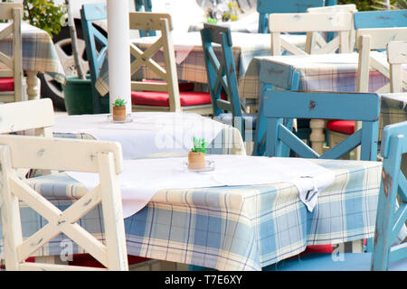 Des tables et des chaises dans un restaurant méditerranéen traditionnel typique sur la terrasse à la lumière bleu et blanc avec nappe à carreaux, détail Banque D'Images