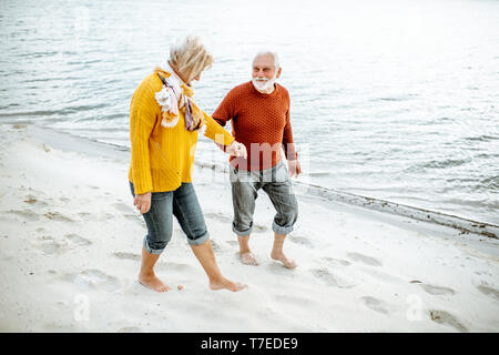 Joli couple vêtus de chandails colorés marche sur la plage de sable, en profitant du temps libre pendant la retraite près de la mer Banque D'Images