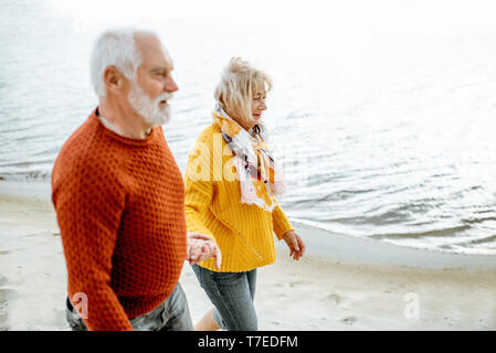 Joli couple vêtus de chandails colorés marche sur la plage de sable, en profitant du temps libre pendant la retraite près de la mer Banque D'Images