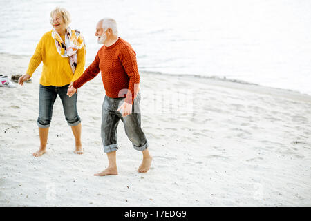 Joli couple vêtus de chandails colorés marche sur la plage de sable, en profitant du temps libre pendant la retraite près de la mer Banque D'Images