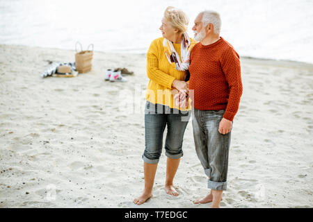 Portrait of a happy senior couple vêtus de chandails colorés serrant sur la plage de sable, en profitant du temps libre pendant la retraite près de la mer Banque D'Images