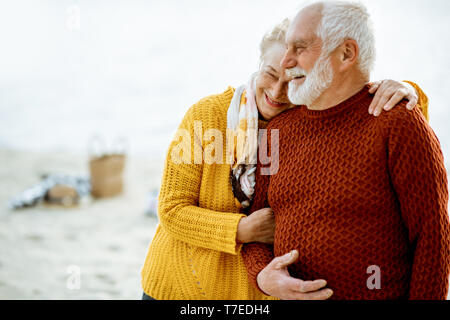 Portrait of a happy senior couple vêtus de chandails colorés serrant sur la plage de sable, en profitant du temps libre pendant la retraite près de la mer Banque D'Images