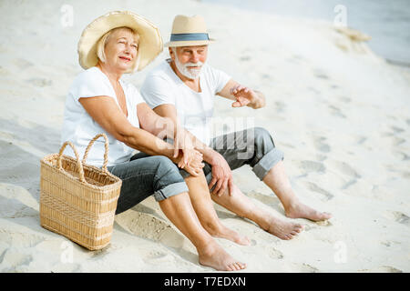 Lovely senior couple relaxing, assis ensemble sur la plage de sable, profitant de leur retraite près de la mer Banque D'Images