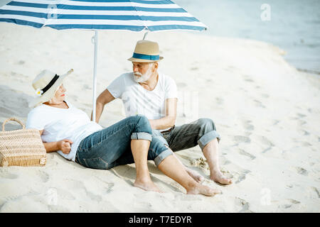 Happy senior couple relaxing, couché ensemble sous parasol sur la plage de sable, profitant de leur retraite près de la mer Banque D'Images