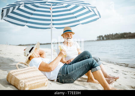 Happy senior couple relaxing, couché ensemble sous parasol sur la plage de sable, profitant de leur retraite près de la mer Banque D'Images