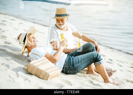 Happy senior couple relaxing, couché avec un verre sur la plage de sable, profitant de leur retraite près de la mer Banque D'Images