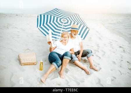 Happy senior couple relaxing, couché ensemble sous parasol sur la plage de sable, profitant de leur retraite près de la mer Banque D'Images