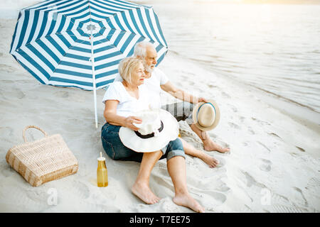 Happy senior couple relaxing, couché ensemble sous parasol sur la plage de sable, profitant de leur retraite près de la mer Banque D'Images