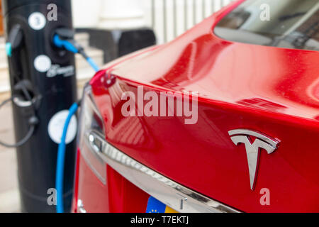 Une voiture rouge Tesla à recharger une station de ravitaillement dans une ville Banque D'Images