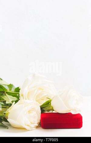 Boîte rouge pour des bijoux avec des roses blanches comme signe d'attention sur fond blanc avec l'exemplaire de l'espace. Shot verticale Banque D'Images